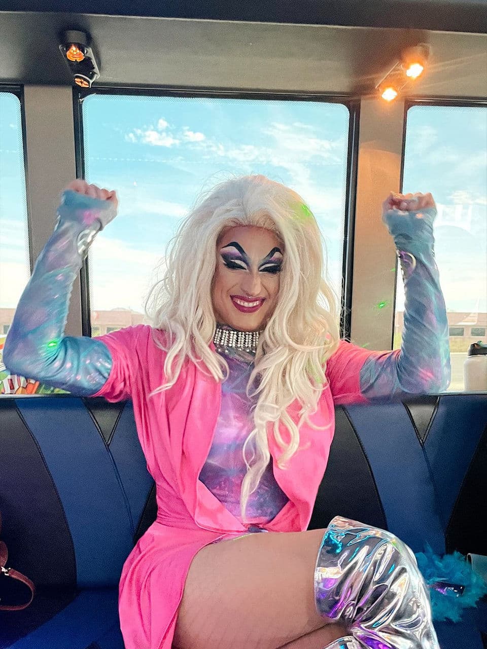 Drag queen in a pink dress and silver boots, celebrating on a bus