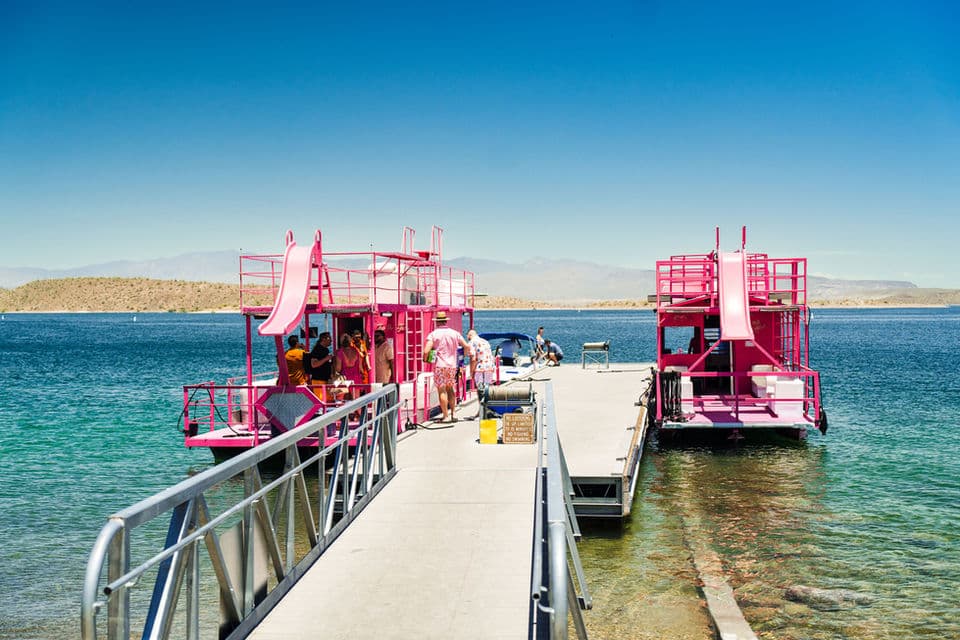 Two pink party boats with waterslides docked at a pier on a clear day